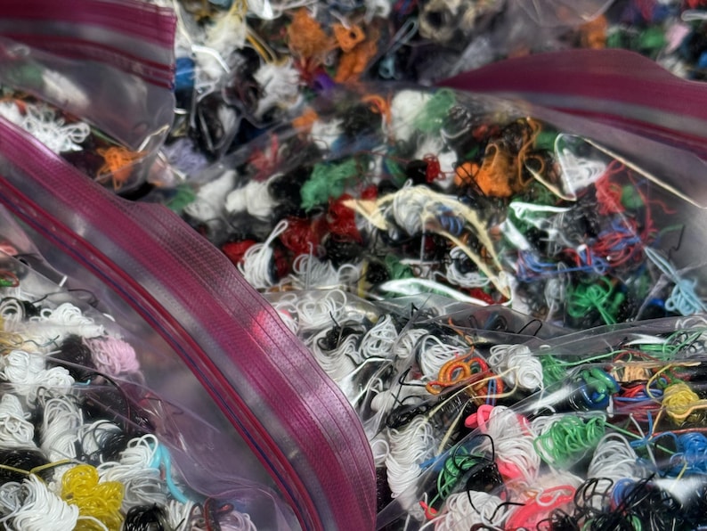 May include: Multiple clear plastic bags filled with colorful embroidery floss. The bags are partially open, revealing the various colors of thread.