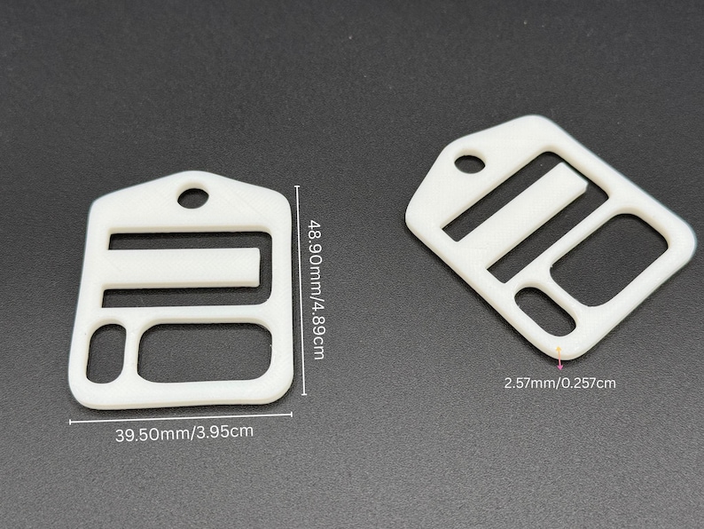 May include: Two white plastic strap adjusters with a rectangular frame, a central horizontal bar, and a circular hole at the top. The dimensions are labeled as 48.90mm by 39.50mm with a thickness of 2.57mm, providing clear technical specifications.