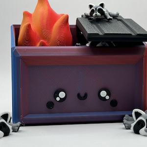 May include: A small, purple, wooden box with a cute cartoon face. The box has a black lid with a raccoon figurine on top. There are three raccoon figurines around the box.