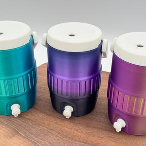 May include: Three small, colorful water coolers with white lids and spouts. The coolers are cylindrical with a ribbed design around the middle. The colors are teal to green, purple to black, and purple to yellow.