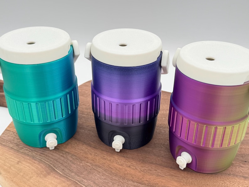 May include: Three small, colorful water coolers with white lids and spouts. The coolers are cylindrical with a ribbed design around the middle. The colors are teal to green, purple to black, and purple to yellow.