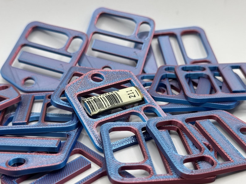 May include: A collection of rectangular plastic buckles with a dual-tone blue and red finish. Each buckle features multiple slots and a circular hole. One buckle in the center displays a small white label with a barcode and the number 211.