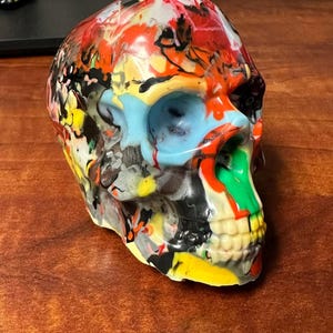 May include: A colorful skull sculpture with a multi-colored paint design. The skull is made of a smooth, glossy material and has a detailed design.