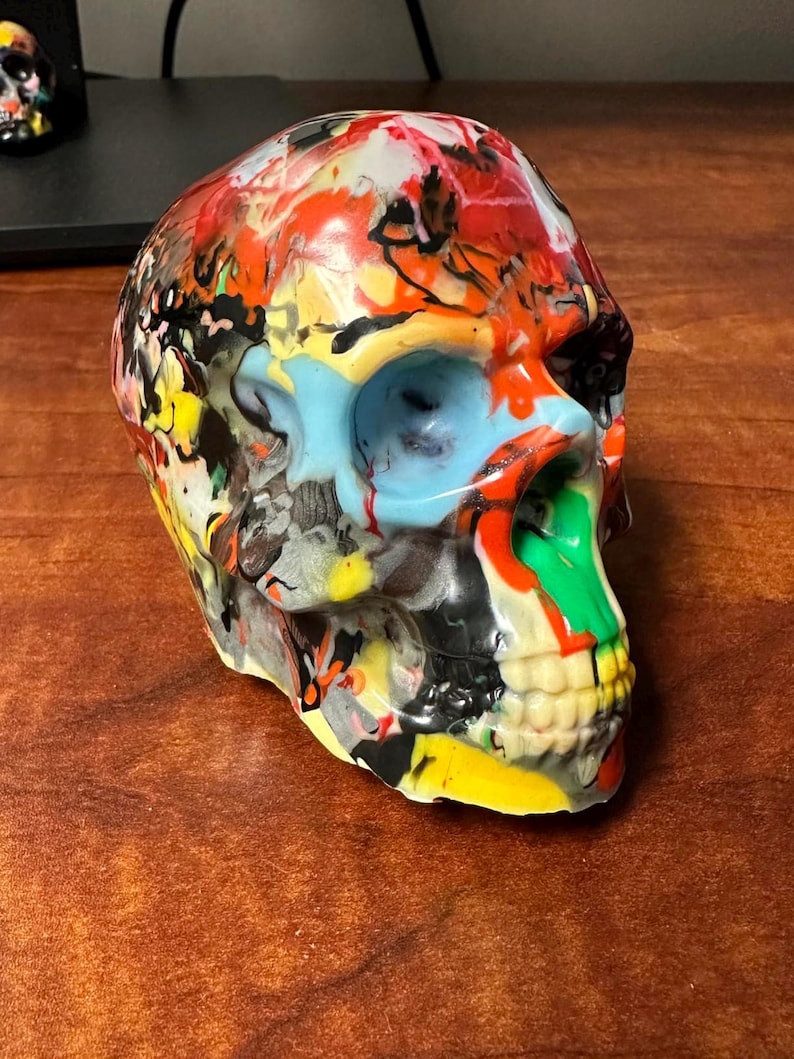 May include: A colorful skull sculpture with a multi-colored paint design. The skull is made of a smooth, glossy material and has a detailed design.