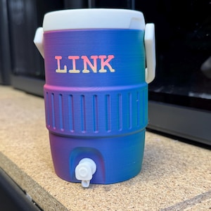 May include: A small, cylindrical cooler with a white lid and handle. The cooler is a gradient of blue and purple with the word "LINK" in orange letters. It has a white spigot at the bottom.