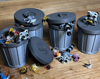 May include: Four gray trash cans with lids, each with a small raccoon figurine inside. The raccoons are in various poses, and some are holding string. The trash cans are on a wooden surface.