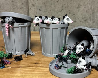 May include: Four gray plastic trash cans with lids, some open, filled with colorful yarn and small, white and black opossum figurines.
