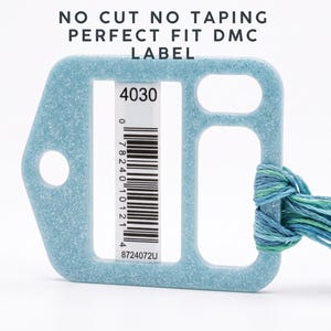 May include: A light blue glittery plastic embroidery floss organizer with a rectangular cutout holding a DMC label with the number 4030 and a barcode. The text NO CUT NO TAPING PERFECT FIT DMC LABEL is visible. Blue and green embroidery thread is attached.