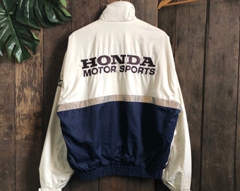 May include: A white and navy blue jacket with a zipper closure and a drawstring waist. The jacket has a reflective stripe across the chest and the words "HONDA MOTOR SPORTS" embroidered on the back.