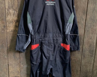 Op de afbeelding: Zwarte werkkleding jumpsuit met rode en grijze accenten. De jumpsuit heeft een ritssluiting en een logo met de tekst "Mitsubishi Motors" op de rug.