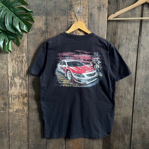 Può includere: Maglietta nera con una stampa grafica di un'auto da corsa rossa e bianca con il testo "ALTIS" sul retro.