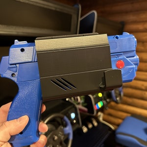 May include: A blue and black 3D printed gun-shaped controller for a video game. The controller has a red button on the side.