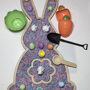 May include: Easter sensory bin featuring a wooden bunny-shaped base filled with colourful rice. Includes toy carrots, eggs, bunnies, a shovel, a spoon, and a green bowl. A fun activity for children.