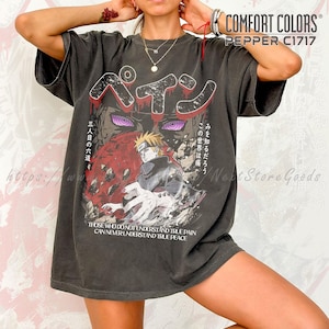 Peut inclure: T-shirt Comfort Colors gris foncé avec un motif comprenant du texte japonais et des illustrations de style anime. Le motif comprend un personnage aux yeux violets et le texte "Those Who Do Not Understand True Pain Can Never Understand True Peace."