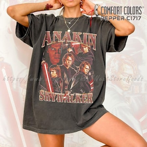 May include: Dark gray Comfort Colors t-shirt featuring a graphic of Anakin Skywalker. The design includes the text "ANAKIN SKYWALKER" in a vintage style. The shirt has short sleeves and a crew neck.