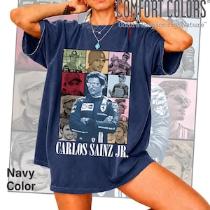 Peut inclure: Un t-shirt bleu marine pr&eacute;sentant un collage de neuf portraits photographiques de Carlos Sainz Jr. dans divers contextes de course. Le texte "CARLOS SAINZ JR." est imprim&eacute; en blanc au bas du graphique. Le t-shirt a un col rond et des manches courtes.