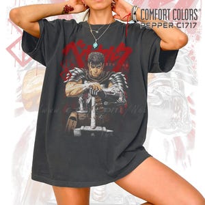 May include: Dark gray Comfort Colors t-shirt featuring a graphic of a warrior with a large sword, the word "BERSERK" in red, and the text "COMFORT COLORS PEPPER C1717". The shirt has a vintage, worn look.