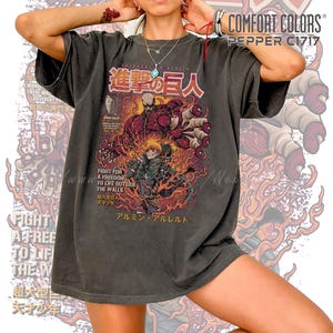 May include: Dark grey Comfort Colors t-shirt featuring a colorful graphic from the anime series Attack on Titan. The design includes Japanese text and illustrations of characters and fiery elements. The shirt has a relaxed fit.
