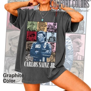 Peut inclure: Un t-shirt gris anthracite &agrave; manches courtes pr&eacute;sentant un collage de neuf portraits photographiques du pilote de Formule 1 Carlos Sainz Jr. Le texte CARLOS SAINZ JR. est imprim&eacute; en lettres capitales blanches sous le graphisme.