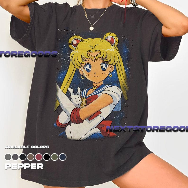 May include: Dark gray t-shirt featuring a colorful anime character illustration. The character has blonde hair, blue eyes, and is wearing a sailor uniform. The text "STOREGOODS" and "NEXTSTOREGOODS" are visible. The shirt is available in several colors.
