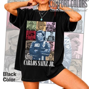 Peut inclure: Un t-shirt noir &agrave; manches courtes pr&eacute;sentant un collage de neuf portraits photographiques du pilote de Formule 1 Carlos Sainz Jr. L'image centrale montre le pilote dans une combinaison de course bleue. Le texte Carlos Sainz Jr. est imprim&eacute; en blanc.