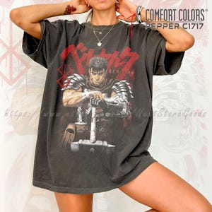 May include: Dark gray t-shirt featuring a graphic of a warrior with a sword and the word "BERSERK" in red. The shirt also has the text "COMFORT COLORS PEPPER C1717".