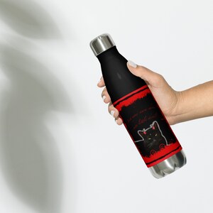 May include: A black stainless steel water bottle with a red and black design. The design features a black cat with red horns and the text "Let ever your own sins, ate little devil!"