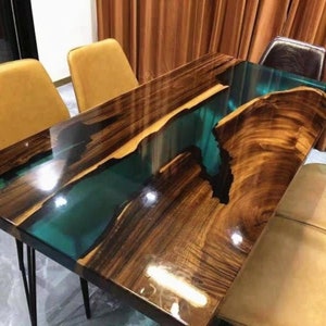 May include: A dark wood dining table with a river of epoxy resin in a teal blue color. The table has a high gloss finish and is surrounded by chairs.