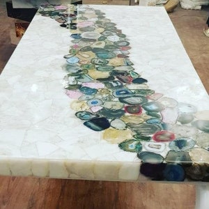 Op de afbeelding: Een wit tafelblad met een decoratief ontwerp van agaatplakken in verschillende kleuren en vormen. De agaatplakken zijn in een gebogen lijn over het tafelblad gerangschikt.