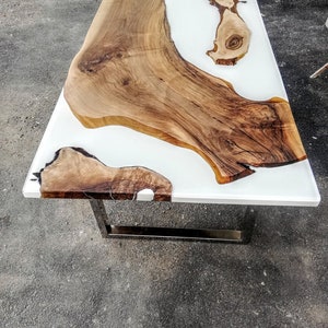 Puede incluir: Una mesa de resina epoxi blanca con una incrustación de madera natural. La mesa tiene un diseño moderno y minimalista con una base de metal.