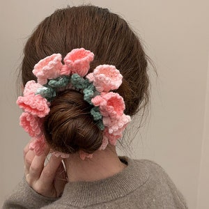 May include: A pink and green crocheted hair scrunchie with flower-shaped embellishments.
