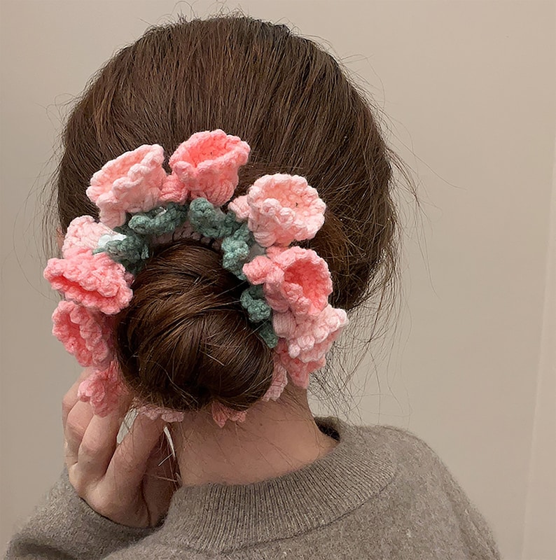 May include: A pink and green crocheted hair scrunchie with flower-shaped embellishments.