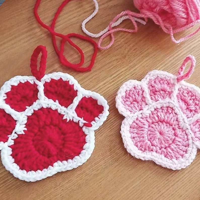 May include: Two crocheted paw print dishcloths, one red with white trim and one pink with white trim.