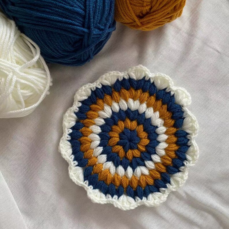 May include: A crocheted coaster with a circular design in white, navy blue, and mustard yellow.