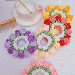 May include: Four crocheted hair scrunchies in different colors. Each scrunchie is made of a circle of crocheted flowers with a center elastic band. The colors are purple, yellow, pink, and red.