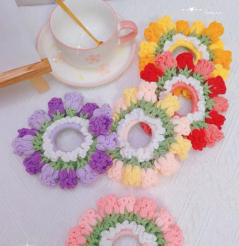 May include: Four crocheted hair scrunchies in different colors. Each scrunchie is made of a circle of crocheted flowers with a center elastic band. The colors are purple, yellow, pink, and red.