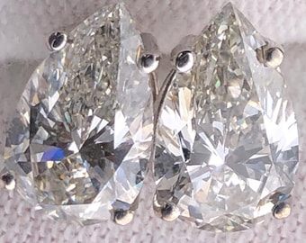Op de afbeelding: Een paar peervormige diamantstud-oorbellen. De heldere, gefacetteerde diamanten schitteren. De oorbellen zijn gezet in een zilverkleurig metaal. Ze liggen op een witte ondergrond.