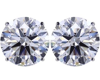 May include: A pair of round, clear diamond stud earrings. The diamonds are set in a silver-coloured metal. The earrings are displayed against a white background. The facets of the diamonds reflect light, creating a sparkling effect.