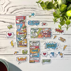 May include: A collection of colorful comic-style stickers with various phrases and words, including "So Good," "Power," and "Amen." The stickers feature speech bubbles, stars, and lightning bolts, with a mix of bold colors and handwritten fonts. The stickers are on a white wooden surface.