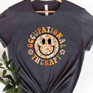 May include: A dark gray t-shirt with a colorful smiley face graphic that says "Occupational Therapy" in a retro font.