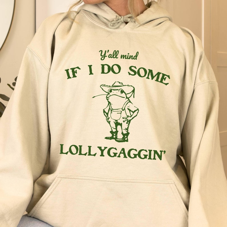 May include: A cream-colored hoodie with a green frog graphic and the text "Y'all mind IF I DO SOME LOLLYGAGGIN'"
