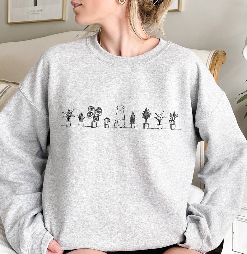 May include: A gray sweatshirt with a black line drawing of a dog sitting in front of a row of potted plants.