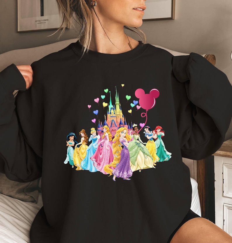 May include: Black sweatshirt featuring a graphic of Disney princesses in front of Cinderella's castle with a pink Mickey Mouse balloon and rainbow hearts.