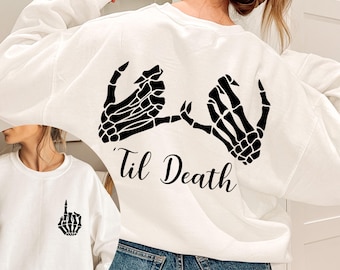 May include: White sweatshirt with a black skeleton hand design and the text "Til Death".
