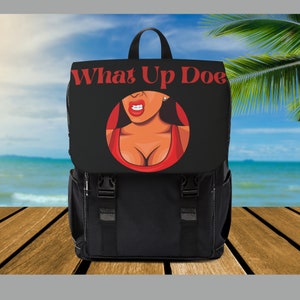 May include: Black backpack with a flap displaying the red text "What Up Doe". The flap also features a cartoon image of a woman in a red top. The backpack has adjustable straps and buckles.