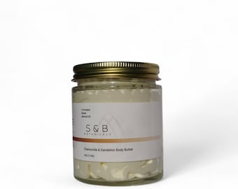 May include: A glass jar with a gold lid filled with a white cream. The label reads "S&B Botanicals Chamomile & Dandelion Body Butter 4oz (113g)"