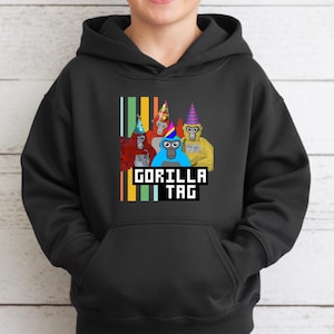 Puede incluir: Sudadera con capucha negra con un gr&aacute;fico de cuatro gorilas de dibujos animados con sombreros de fiesta. El texto "GORILLA TAG" se muestra en una fuente pixelada debajo de los gorilas, con rayas verticales en el lado izquierdo.