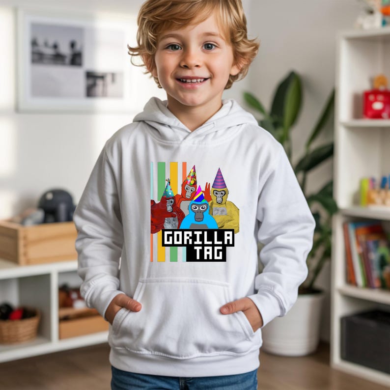 Puede incluir: Sudadera con capucha blanca con un gr&aacute;fico de gorilas de dibujos animados con sombreros de fiesta. El texto "GORILLA TAG" est&aacute; impreso debajo en una fuente pixelada. La sudadera tiene un bolsillo delantero y una capucha con cord&oacute;n.
