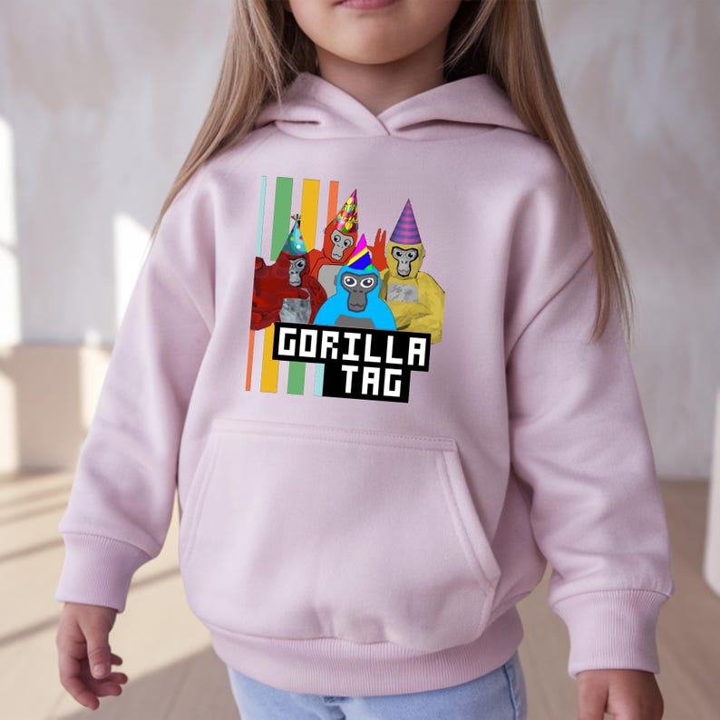 Puede incluir: Sudadera con capucha rosa claro con un gr&aacute;fico de cuatro gorilas de dibujos animados con sombreros de fiesta. Los gorilas son rojos, azules y amarillos. El texto "GORILLA TAG" est&aacute; debajo.
