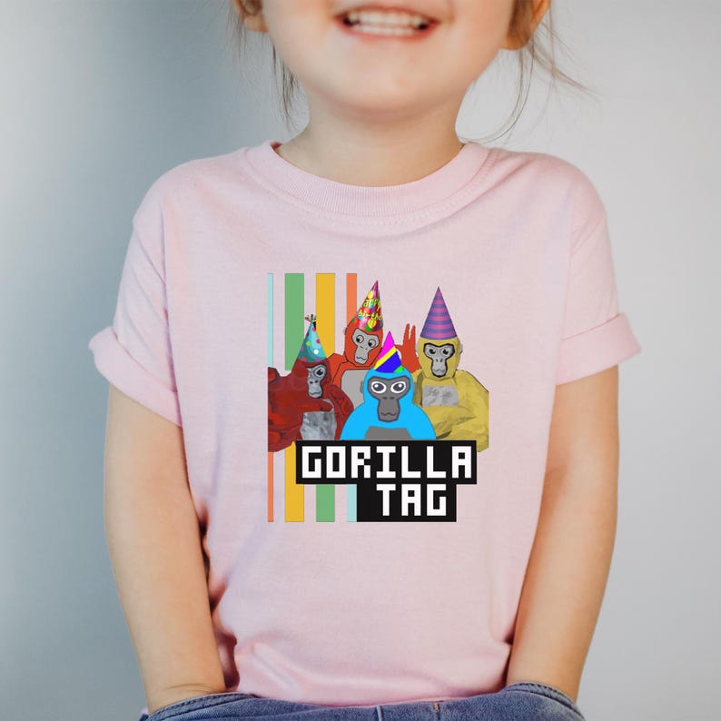 Puede incluir: Una camiseta rosa claro con un gr&aacute;fico de cuatro gorilas de dibujos animados con sombreros de fiesta. Los gorilas son rojos, naranjas, azules y amarillos. El texto "GORILLA TAG" est&aacute; en negro, con fuente pixelada.